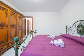 Ein Schlafzimmer mit einem Bett, einem Holzschrank und einem grünem Metall-Kopfteil.