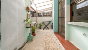 A narrow courtyard with a tiled floor, potted plants, a small table, and a window with a view of a building. - Casa Vacanze 'EliFra' with Private Terrace, Garden, and Balcony (San Giovanni Suergiu)
