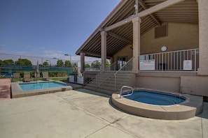 A covered swimming pool area with a small hot tub, stairs leading to a building, and a fenced tennis court in the background. - Sports Village | All Amenities Included | Q9 (Saint George)