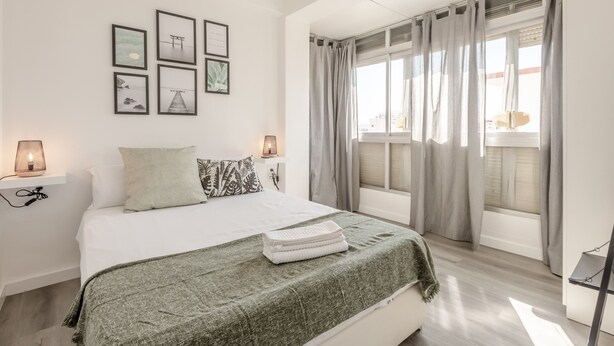 Ein Schlafzimmer mit Bett, Nachttischlampen, einem Fenster mit Vorhängen und Wandbildern.