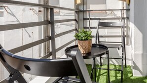 Ein Balkon mit einem Metallstuhl, einem kleinen runden Tisch und einem gewebten Korb mit einer Pflanze.