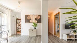 Ein modernes Wohnzimmer mit Holzboden, einem weißen Sofa, einem Glastisch und einem Fernseher auf einem weißen Schrank.