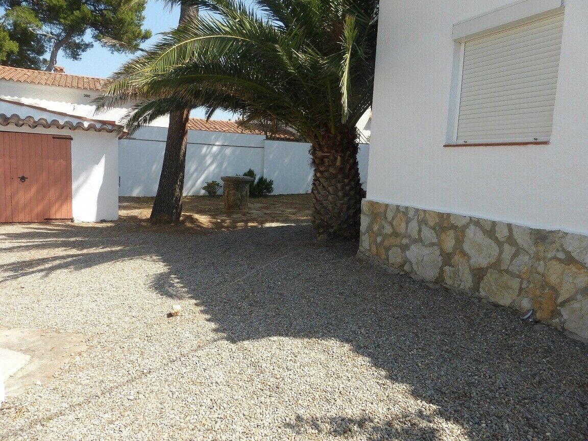 Un edificio con pared de piedra, una palmera y un camino de grava.