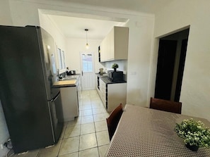 A kitchen with a refrigerator, cabinets, a dining table, and chairs. - Holiday Home 'El Pozo - 400m from Riells Beach' with Terrace, Garden and Balcony (L'Escala)