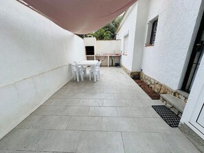 A patio with a table and chairs, a small kitchen area, and a white exterior wall. - Holiday Home 'El Pozo - 400m from Riells Beach' with Terrace, Garden and Balcony (L'Escala)
