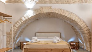A bedroom with a stone arch ceiling, a wooden bed, and a bedside table with a lamp.