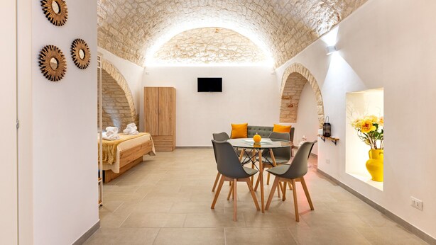 A room with a stone ceiling, a bed with towels, a dining table with chairs, and a vase with flowers.