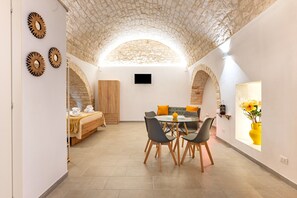 A room with a stone ceiling, a bed with towels, a dining table with chairs, and a vase with flowers. - Studio 'La Pizzicata' with Wi-Fi and Air Conditioning (Ostuni)