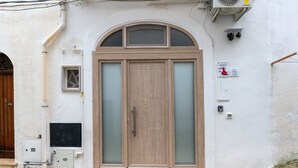A building with a large wooden door, a small window, and a tiled entrance area.