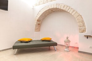 Ein Zimmer mit einem Bett, einer gewölbten Steinwand, einem kleinen Tisch und einer dekorativen Lampe.