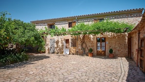 A courtyard with stone flooring, a building with a tiled roof, and potted plants.