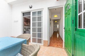 Une pièce avec une table, des chaises, une porte verte et un couloir menant à une autre pièce.