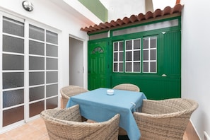 Une terrasse avec une table et des chaises, une porte verte et un mur blanc.