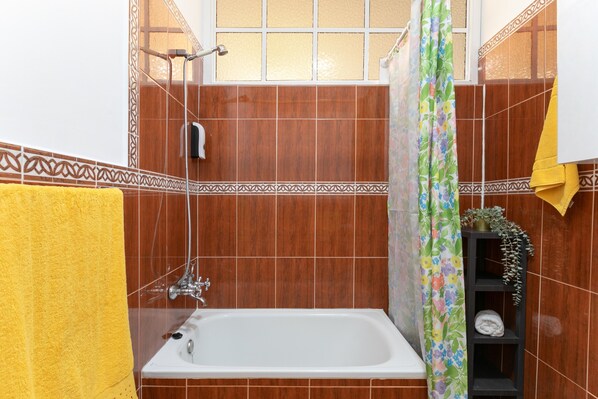 Een badkamer met een bad, douche en een plank met handdoeken.