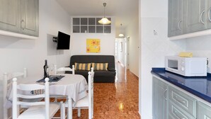 A modern kitchen with a microwave, a dining table with chairs, a sofa, and a TV mounted on the wall.