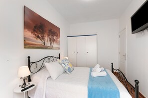 Une chambre à coucher avec un lit, une table de chevet, une télévision, une armoire et un tableau.