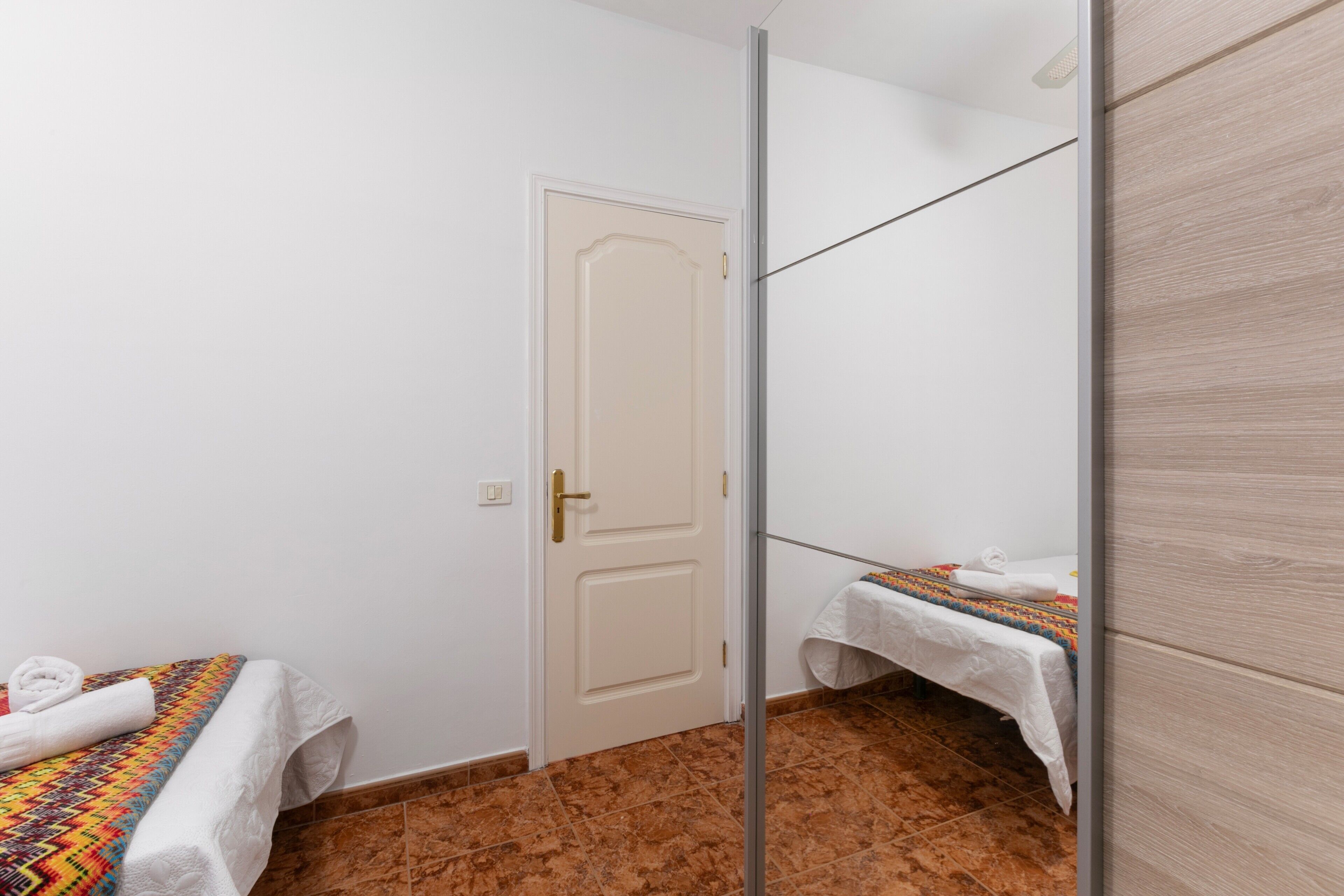 Una habitación con dos camas, una puerta blanca y un espejo.