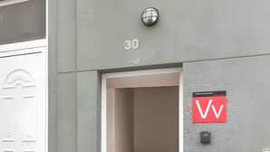 A building entrance with a door marked '30', a staircase leading inside, and a red sign with 'VV' on the wall.