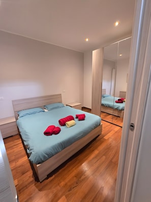 Una camera da letto con un letto, pavimento in legno e uno specchio.