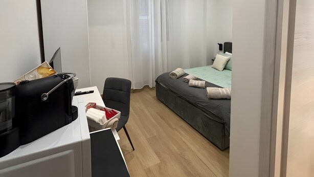 Et moderne hotelværelse med seng, skrivebord med computer, stol og et klimaanlæg.