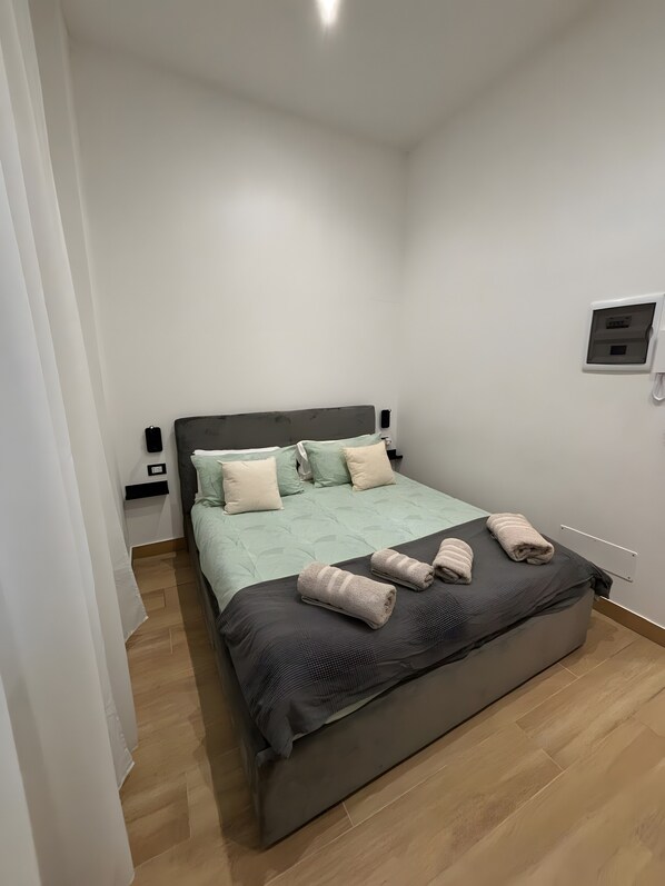 A neatly made bed with pillows, a bedside table, and a wall-mounted device.