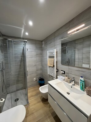 Une salle de bain moderne avec une douche à parois de verre, des toilettes, un bidet et un grand miroir.