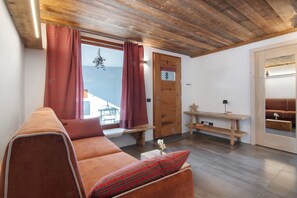 A cozy room with a wooden ceiling, a sofa with a plaid pillow, a wooden door with a window, and a small table with a lamp. - Apartment 'Nadia' with Lake View, Private Terrace and Wi-Fi (Verceia)
