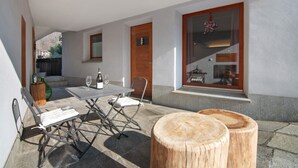 A patio with a table and chairs, a wooden stool, and a window with a view of the interior.