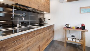 A modern kitchen with wooden cabinetry, a stainless steel sink, and a wooden table with a kettle and coffee maker.