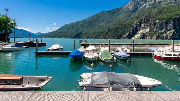 A marina with boats docked, a wooden deck, and a mountainous backdrop.