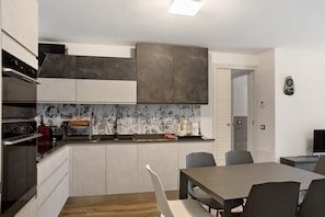 Une cuisine moderne dotée d’appareils électroménagers intégrés, un coin repas avec une table et des chaises, et un petit espace salon.