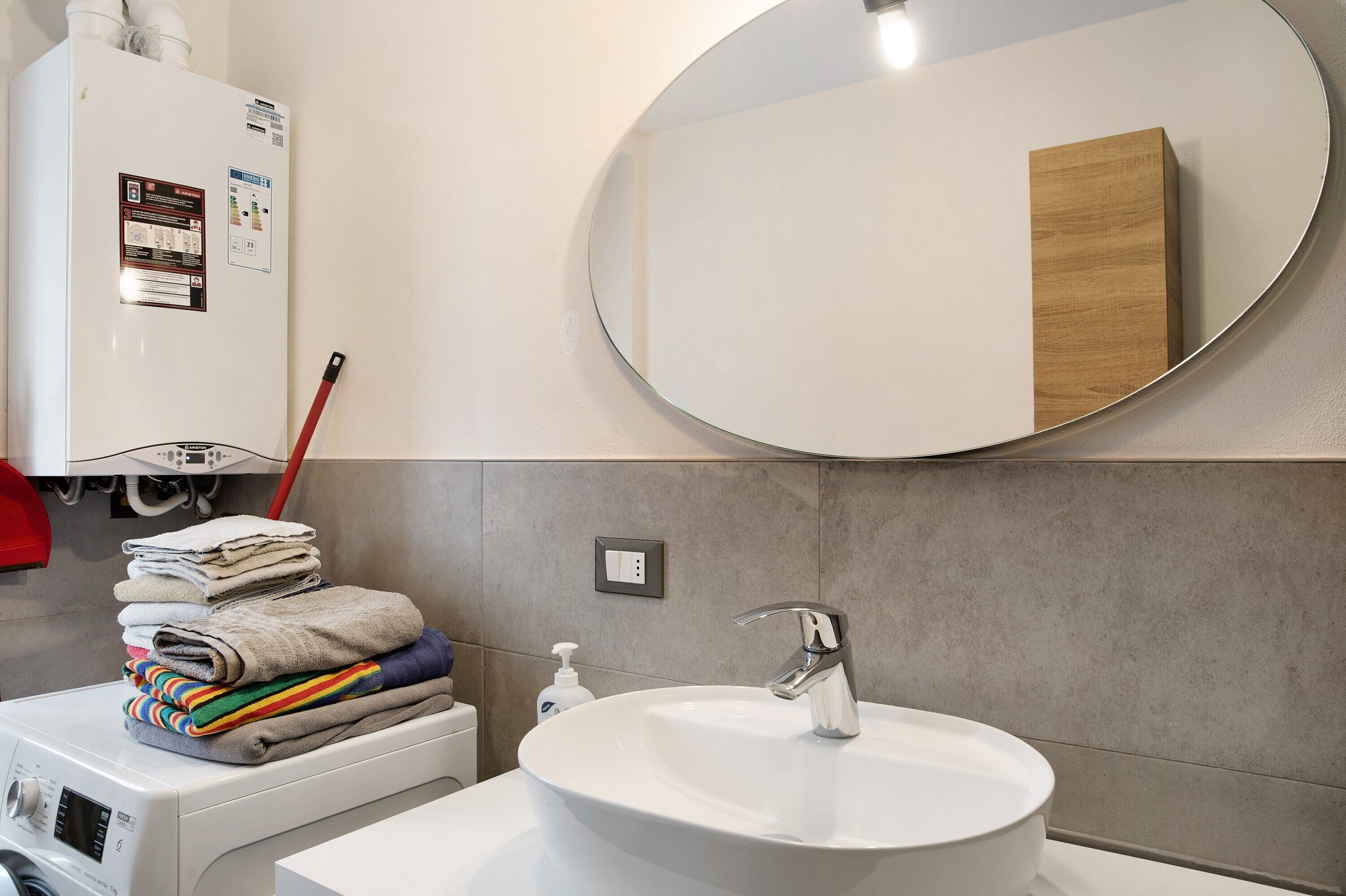 A bathroom with a sink, mirror, towel stack, and a washing machine.