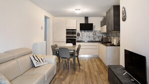 A modern kitchen with a dining area, a TV, and a sofa with a decorative pillow. - Apartment 'Giorgia - Caspoggio' with Mountain View, Shared Garden and Balcony (Caspoggio)