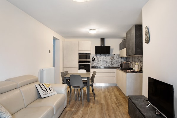 Une cuisine moderne avec un coin repas, un téléviseur et un canapé agrémenté d  ’un coussin décoratif.