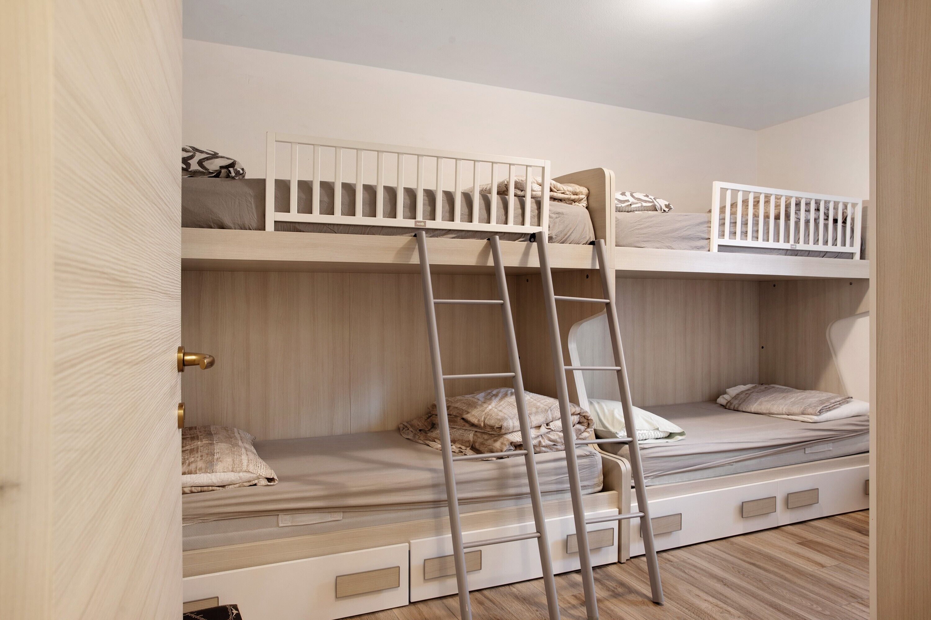 Een slaapkamer met een stapelbed, een ladder, houten wanden en een deur.