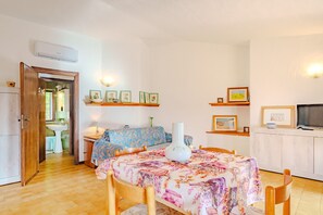 Una habitación con una mesa de comedor de madera, sillas, un sofá, un televisor y un armario.