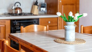 Una cocina con salpicadero blanco de azulejos, armarios de madera, una estufa y un jarrón con flores blancas sobre una mesa.
