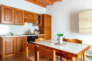 Een keuken met houten kasten, een betegeld aanrecht, een eettafel met stoelen en een vaas met bloemen.