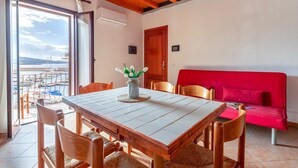 Un comedor con mesa y sillas, un sofá rojo y vistas al mar a través de amplios ventanales.