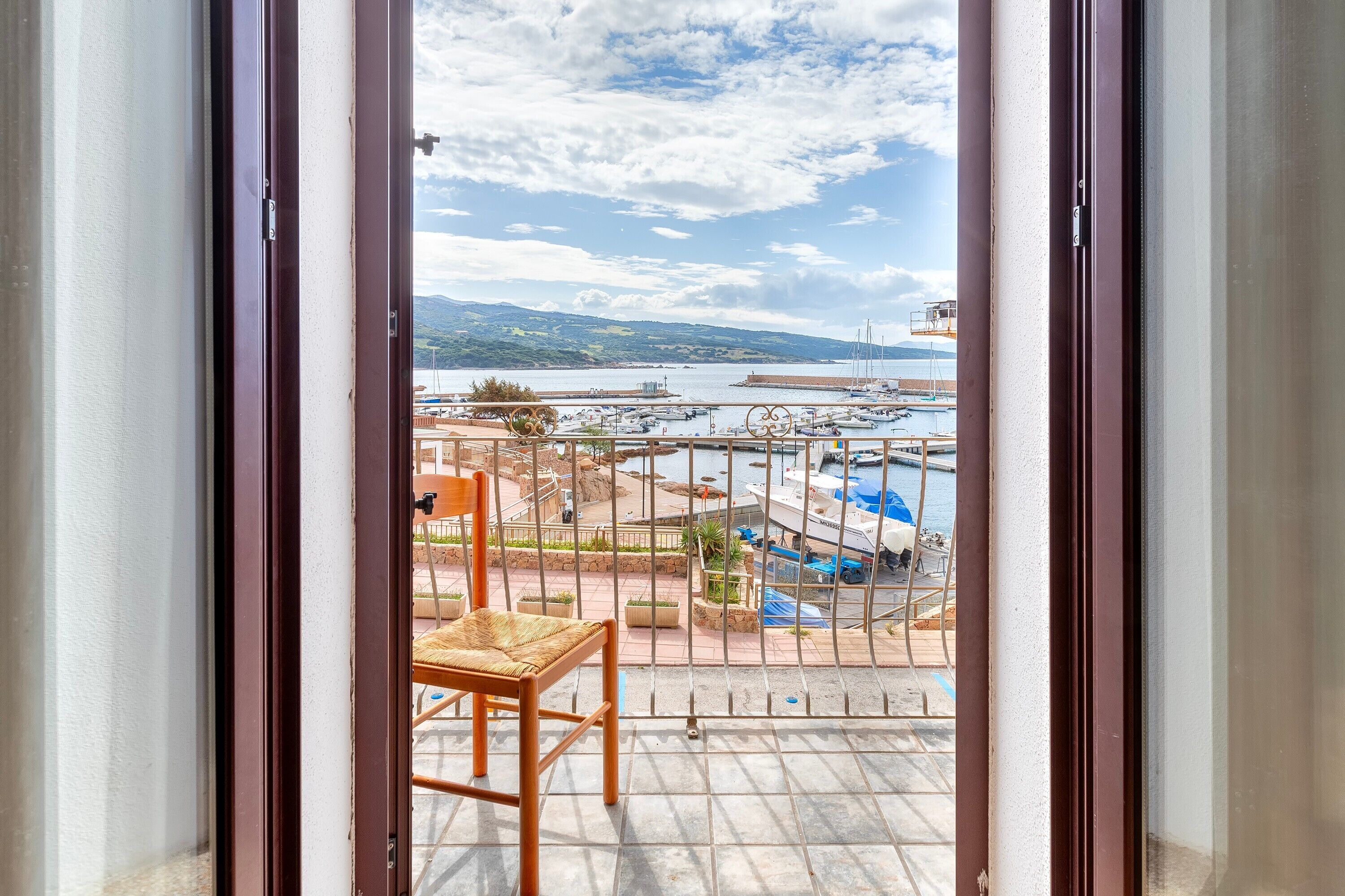 Un balcón con vistas a un puerto deportivo, una silla y piso de baldosas.