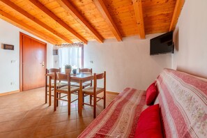 Una habitación con techo de madera, una cama con almohadas rojas, un televisor montado en la pared y un comedor con sillas y una mesa.