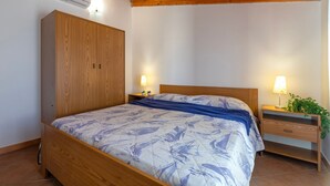 Un dormitorio con una cama de madera, una mesita de noche con lámpara, un armario de madera y un techo con vigas de madera.