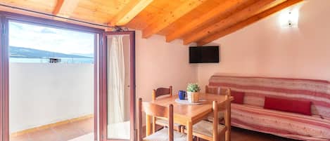 A wooden ceiling, a dining table with chairs, a sofa, a TV, and a view through a glass door.
