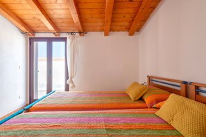 Un dormitorio con techo de madera, una cama con ropa de cama colorida y un ventanal con cortinas.