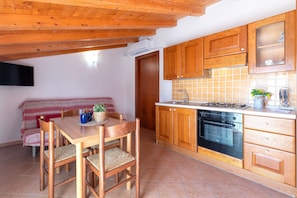 Een keuken met houten kastjes, een fornuis en een eethoek met een tafel en stoelen.