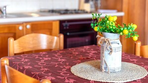 Ett lantligt kök med träskåp, ett matbord med en vävd bordsduk och en vas med gula blommor.