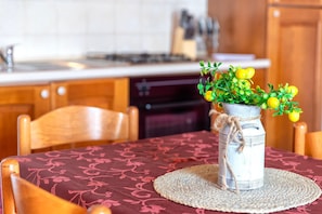 A rustic kitchen with wooden cabinets, a dining table with a woven placemat, and a vase with yellow flowers.