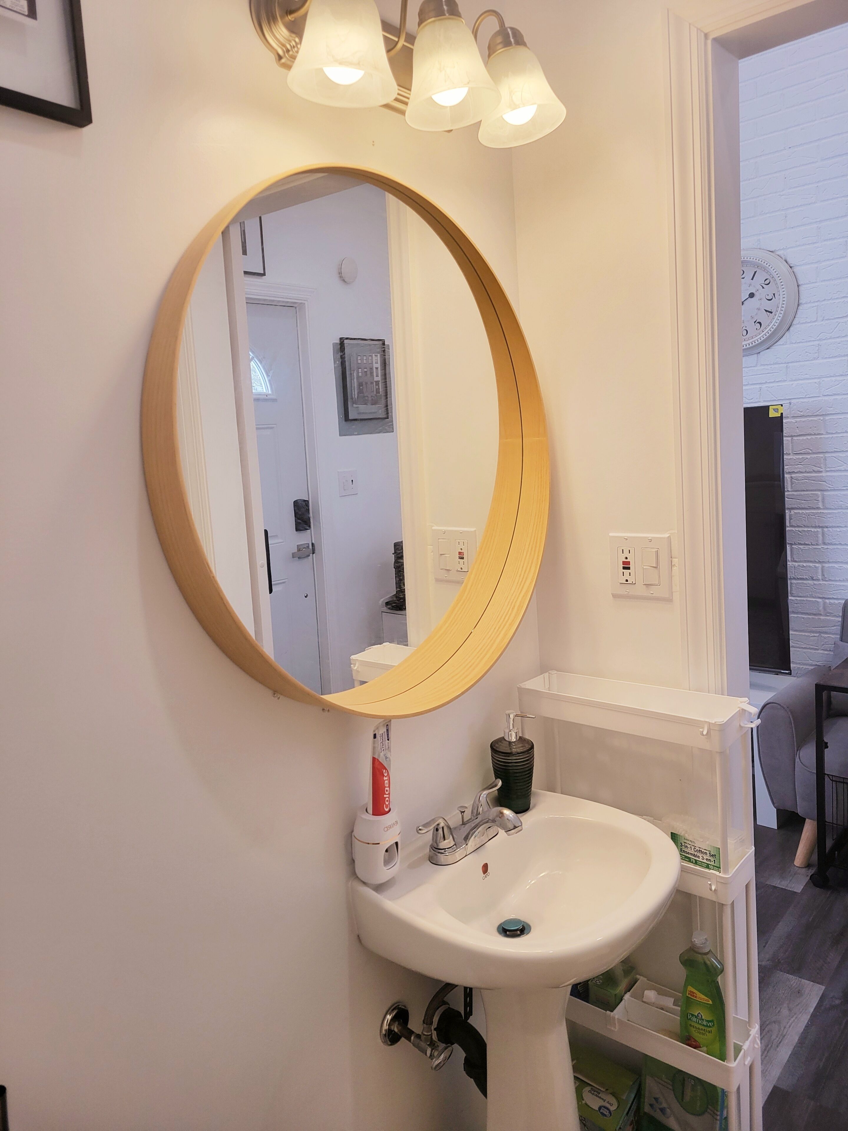 Une salle de bain avec un lavabo blanc, un miroir rond et un luminaire placé au-dessus du miroir.