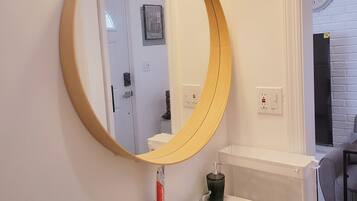 Une salle de bain avec un lavabo blanc, un miroir rond et un luminaire placé au-dessus du miroir.