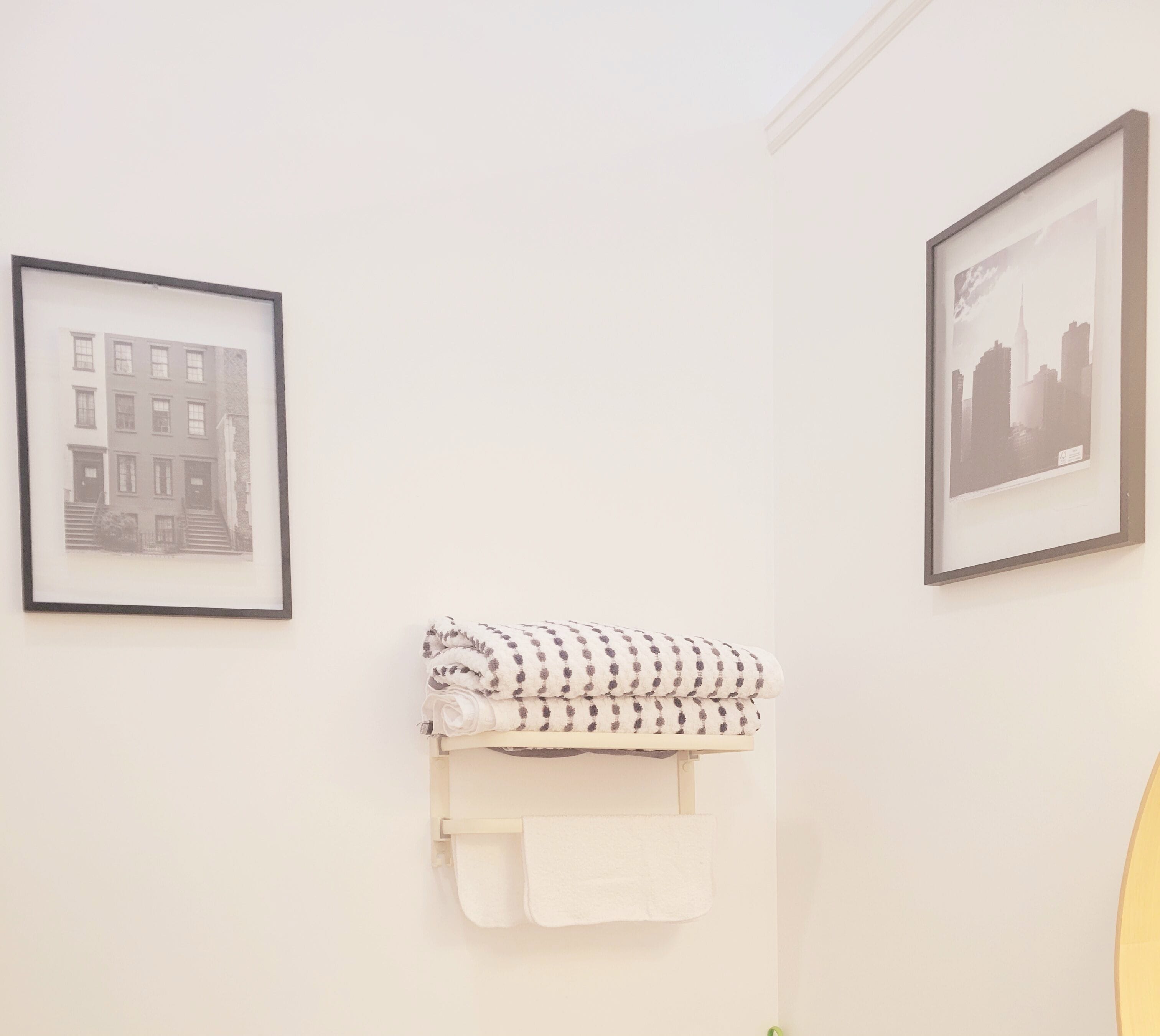 A bathroom with a towel rack holding a folded towel and a rolled towel, framed pictures of a building and a cityscape on the walls.